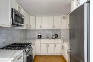 uma cozinha com armários brancos e um frigorífico de aço inoxidável em UES 1br w gym doorman walk to central park NYC-1332 em Nova York