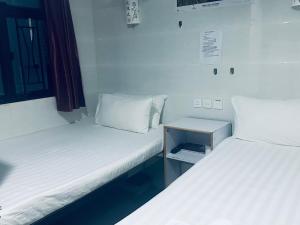 KATHMANDU GUEST HOUSE في هونغ كونغ: سريرين في غرفة صغيرة ذات أغطية بيضاء