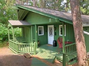 a green cabin with a porch and a red chair at Pinehaven of Baraboo in Baraboo