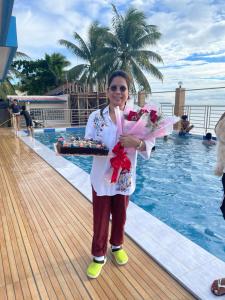 Una donna in piedi accanto a una piscina con una torta e dei fiori di LUMBAYAN BEACH RESORT a Dawis