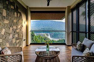 ein Wohnzimmer mit einem Tisch und einem großen Fenster in der Unterkunft Flora Misty Falls Athirappilly in Athirappilly