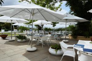 un patio con mesas, sillas blancas y sombrillas en The Devon Valley Hotel, en Stellenbosch