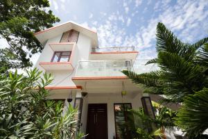 a white house with a balcony and palm trees at Marari Anns Casa Beach Homestay in Mararikulam