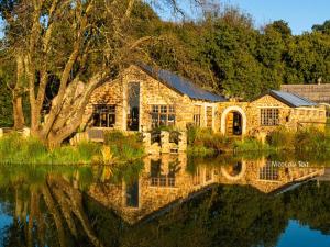 une maison en pierre avec une réflexion dans l'eau dans l'établissement Flitwick Ranch, à Swartberg