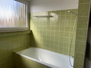 baño de azulejos verdes con bañera y ventana en Hotel Ditzingen, en Ditzingen