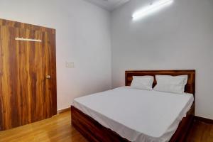 a bedroom with a bed with white sheets and a wooden door at OYO Hotel Pitra Chaaya Hotel And Restaurant in Mathura