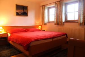 1 Schlafzimmer mit einem Bett mit roter Bettwäsche und 2 Fenstern in der Unterkunft Stöcklgut Apartment 