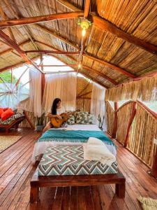 Villa Sonia Eco-Hostel في Gigante: امرأة تجلس على سرير في غرفة مع غيتار