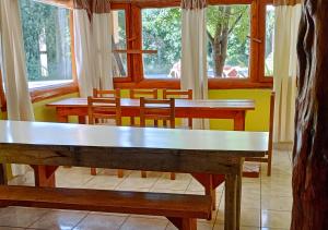 un comedor con mesas, sillas y ventanas en Corinto Hostel en El Bolsón