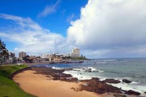 une plage avec des bâtiments et l'océan avec des vagues dans l'établissement Apartamento em frente ao mar, à Salvador