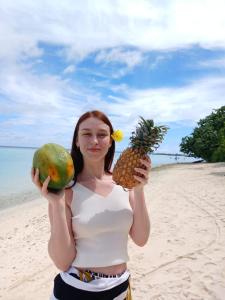a woman holding a pineapple and a melon on the beach at Sunrise Inn in Thoddoo