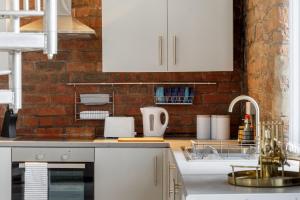 una cocina con armarios blancos y una pared de ladrillo en Broadgate Penthouse Apartment, en Bradford