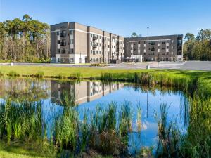 an apartment building with a reflection in a pond at WaterWalk Jacksonville - Deerwood Park in Jacksonville