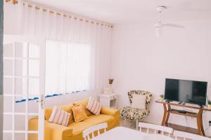 ein Wohnzimmer mit einem gelben Sofa und einem TV in der Unterkunft Casa com churrasqueira e 3 quartos - Centro in Búzios