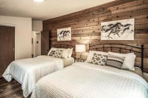 two beds in a bedroom with wooden walls at Peak In The Pines in Ruidoso