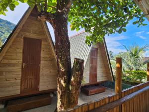 um edifício de madeira com duas portas ao lado de uma árvore em Raio de Sol pousada & camping em Abraão
