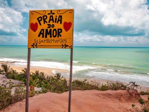 un cartel amarillo en una playa con el océano en Pousada Praia do Amor Pipa, en Pipa