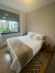 um quarto com uma cama grande e uma janela em Apart moderno 3 suites 2 vagas de garagem e quadra do mar em Itapema