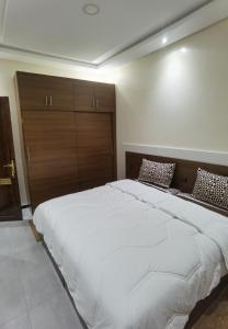 een slaapkamer met een groot wit bed met een houten hoofdeinde bij شقق مفروسة المشور in Laayoune