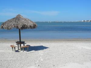 a umbrella and two benches on a beach at Affordable Two Bedroom Tropical Condo - Private Beach, Pools, Hot Tub in St. Petersburg