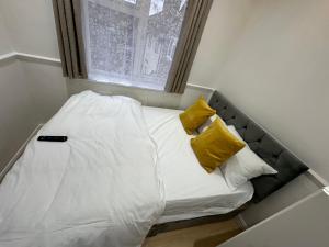 Cama pequeña con almohadas amarillas y ventana en 3rd Studio Flat With Private Toilet and Bathroom Setup For Family Enjoyment 134 Keedonwood Road Bromley, en Bromley