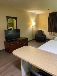 a hotel room with a bed and a tv and a chair at Suburban Studios in Auburn Hills
