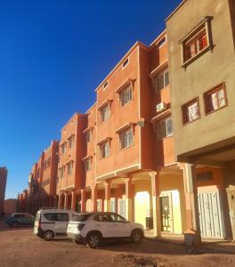 deux voitures garées devant un bâtiment dans l'établissement Appartement Sariq Ouarzazate, à Ouarzazate