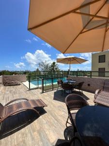 a patio with tables and chairs and an umbrella at Flat Porto do Galo in Porto De Galinhas
