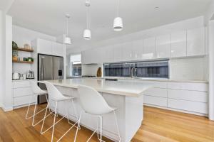 a white kitchen with white chairs and a counter at CasaRona Del Mar in Inverloch