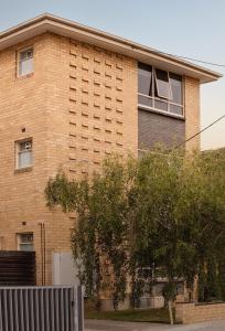 un edificio de ladrillo con un árbol delante de él en MAC South Yarra by Melbourne Apartment Collection, en Melbourne