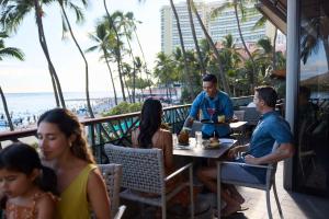 a group of people sitting at a table at a restaurant on the beach at OUTRIGGER Waikiki Beach Resort in Honolulu