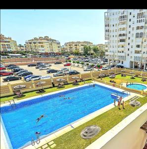 une grande piscine à côté d'un parking avec voitures dans l'établissement Primera linea playa valdelagrana vistas al mar, à El Puerto de Santa María