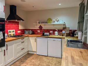 cocina con armarios blancos y paredes de ladrillo rojo en Byre Cottage en Billingshurst