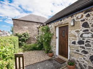 uma casa de pedra com uma porta de madeira e flores em Newton Cottage em Leitholm