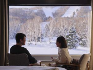 Shigakogen Prince Hotel في يامانوتشي: رجل وامرأة يجلسان على الكراسي وهما ينظران من النافذة