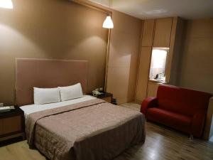 um quarto de hotel com uma cama e uma cadeira vermelha em 金利星精品旅館 em Nan-p'ing