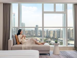 una mujer sentada en un sofá en una habitación con ventana en Sheraton Guangzhou Hotel, en Guangzhou