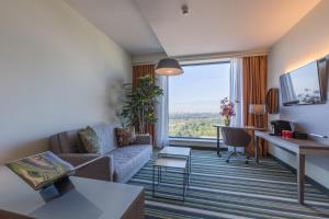 a living room with a couch and a large window at Leonardo Royal Hotel Amsterdam in Amsterdam