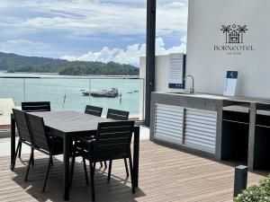 a table and chairs on a deck with a boat in the water at Borneotel The Shore KK by CHG in Kota Kinabalu