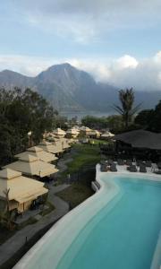 a resort with a pool and umbrellas and a mountain at Toteme Glamping and Hot Spring Kintamani in Kubupenlokan