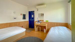 een kamer met 2 bedden, een bureau en een blauwe deur bij Backpacker's Home in Seogwipo