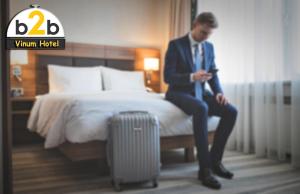 un uomo in giacca e cravatta seduto su un letto con una valigia di Vinum Hotel a Tbilisi City