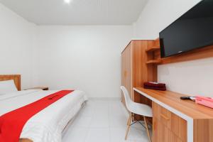 Schlafzimmer mit einem Bett und einem Schreibtisch mit einem TV in der Unterkunft RedDoorz Plus Syariah near Mall Boemi Kedaton Lampung in Kedaton