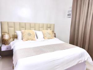 um quarto com uma cama grande com lençóis brancos e almofadas em Cozy Condo Unit in Puerto Princesa City near PPS Airport em Puerto Princesa