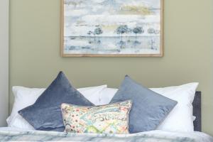 een bed met blauwe kussens en een schilderij aan de muur bij Dickens House- 3BR 15min close to Gatwick in Crawley