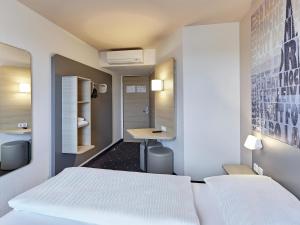 a bedroom with two white beds and a desk at B&B Hotel Köln-West in Cologne