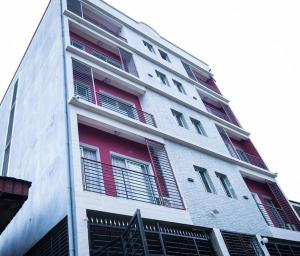 a tall white building with red shuttered windows at Appart ELRESIDANCIEL Palmiers 2 in Douala
