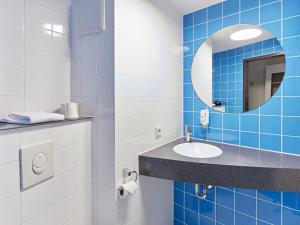 ein blau gefliestes Bad mit einem Waschbecken und einem Spiegel in der Unterkunft B&B Hotel Köln-Messe in Köln