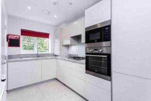 a white kitchen with white cabinets and black appliances at Cosy 3 bed house close to Gatwick Airport in Ifield