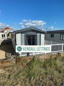 una pequeña casa blanca con un cartel que lee los ajustes de Kendall en Sea View Lodge, en Selsey